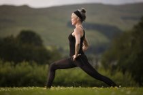 Reife Frau praktiziert Yoga-Krieger Pose im Feld — Stockfoto