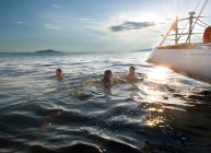Three people swimming next to sailboat — Stock Photo