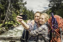 Teenager-Mädchen und junge Wanderin umarmen sich auf Fußgängerbrücke für Smartphone-Selfie, Red Lodge, Montana, USA — Stockfoto