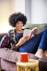 Reife Frau entspannt sich auf Sofa beim Lesen von Buch — Stockfoto