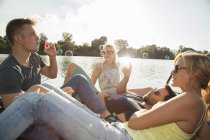 Quattro giovani amici adulti che soffiano bolle sul molo lungo il fiume — Foto stock