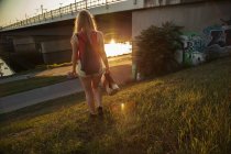 Вид сзади на молодую женщину, идущую рядом с мостом и рекой — стоковое фото