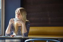 Молода жінка сама в кафе п'є каву — стокове фото