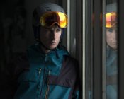 Man wearing helmet and ski goggles looking through window — Stock Photo