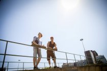 Two men, holding skateboards, leaning on railings, low angle view — Stock Photo
