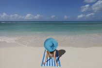 Junge Frau entspannt am Strand mit blauem Sonnenhut — Stockfoto