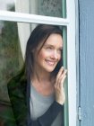 Женщина смотрит в окно, улыбаясь — стоковое фото