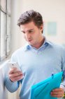 Young businessman reading texts on smartphone in office — Stock Photo