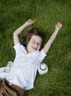 Menino deitado na grama com os braços levantados e rindo — Fotografia de Stock