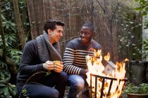 Two young men crouching in front of garden fire with coffee — Stock Photo