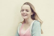 Портрет усміхненої дівчини з довгим світлим волоссям перед стіною — стокове фото