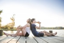 Young couple relaxing on jetty, sitting back to back — Stock Photo