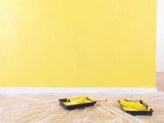 Ролики краски на полу рядом с желтой окрашенной стеной — стоковое фото