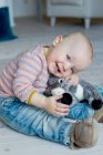 Portrait of baby girl sitting on living room floor hugging soft toy — Stock Photo