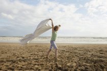 Girl holding up blanket on breezy beach, Camber Sands, Kent, UK — Stock Photo