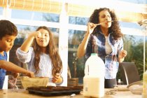 Mother and children tasting cake mixture in kitchen — Stock Photo