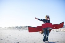 Garçon debout avec avion jouet et pointant sur la plage — Photo de stock