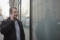 Hombre adulto medio hablando en el teléfono inteligente, mientras que las compras ventana - foto de stock