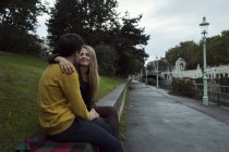 Jovem casal sentado cara a cara na parede do parque — Fotografia de Stock