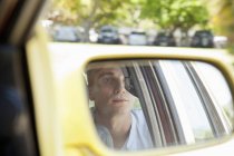 Reflection of young man in rear view mirror — Stock Photo