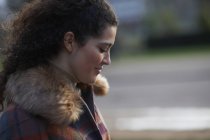 Side view of curly haired woman wearing tartan fur trim coat looking down smiling — Stock Photo