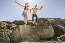 Couple à l'extérieur, tenant la main, sautant de la roche sur le sable — Photo de stock