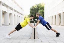 Men stretching on divider in alley between office buildings — Stock Photo