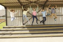 Пять мальчиков и девочек прыгают в воздухе на трибуне стадиона — стоковое фото