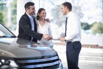 Mid adult couple shaking hands with salesman in car dealership — Stock Photo