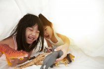 Joven chino chico y chica en la cama jugando con sus juguetes debajo de las sábanas - foto de stock