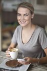 Retrato de jovem mulher sentada no café com xícara de café e celular — Fotografia de Stock