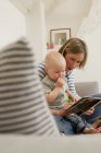 Reife Mutter und kleine Tochter lesen Bilderbuch auf Wohnzimmersofa — Stockfoto