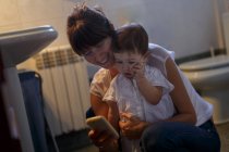 Metà donna adulta e figlia bambino guardando verso il basso lo smartphone in bagno — Foto stock