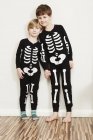 Dois meninos vestidos com roupas de esqueleto olhando na câmera contra a parede branca — Fotografia de Stock