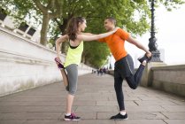 Male and female city runners warming up — Stock Photo