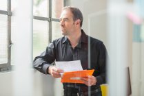Бизнесмен читает документы и смотрит в окно офиса — стоковое фото