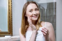 Woman applying face cream looking at camera and smiling — Stock Photo
