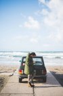 Hombre con coche vintage aparcado en la playa leyendo textos de teléfonos inteligentes, Sorso, Sassari, Cerdeña, Italia - foto de stock