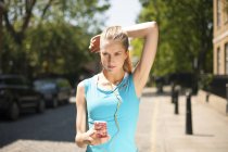 Runner listening to music in smartphone on street, Wapping, London — Stock Photo