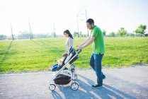 Mid adult couple and toddler daughter in pushchair strolling in park — Stock Photo