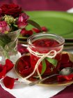 Jar of homemade redcurrant jam and rose petals on table — Stock Photo