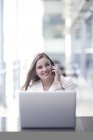 Junge Geschäftsfrau nutzt Laptop und chattet auf Smartphone im Konferenzzentrum — Stockfoto