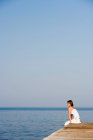 Жінка сидить на пірсі біля моря — стокове фото