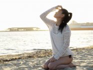 Mujer joven arrodillada en la playa soleada, Port Melbourne, Melbourne, Victoria, Australia - foto de stock