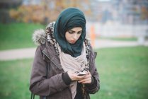 Молодая женщина в парке пишет смс на смартфоне — стоковое фото