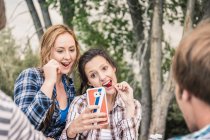 Вид через плечо на молодых женщин, которые едят вишню и делают селфи на смартфоне — стоковое фото