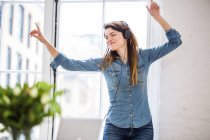 Young woman with eyes closed dancing in front of city apartment window — Stock Photo