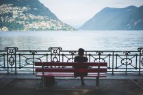 Rear view of silhouetted woman on park bench looking out at Lake Lugano, Switzerland — Stock Photo