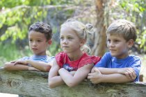Tres niños apoyados en la valla y mirando hacia otro lado - foto de stock