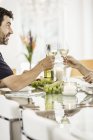 Mature couple sitting at table, holding wine glasses, making toast — Stock Photo